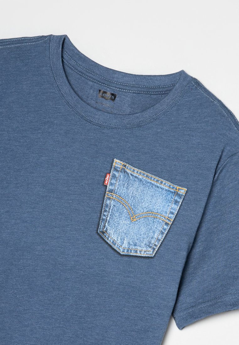 Camiseta de algodón azul con cuello redondo, que presenta un bolsillo de mezclilla azul claro con detalles de costura amarilla.
