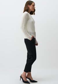 Witte gebreide trui met gestreept patroon, gecombineerd met zwarte cropped broeken en zwarte schoenen met puntige neuzen. Minimalistisch ontwerp en getailleerde silhoeet.
