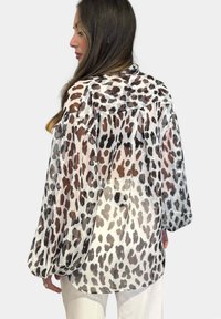 Blusa trasparente bianca con stampa leopardata marrone e nera. Include una vestibilità ampia, spalle scese e un orlo arrotondato.