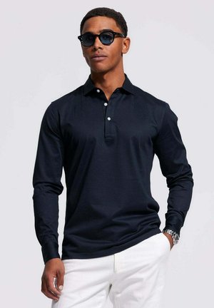 Donker lange mouwen polo shirt met knoopkraag, gestructureerde stof en witte knopen, gecombineerd met witte broeken. Soepele, aansluitende pasvorm.