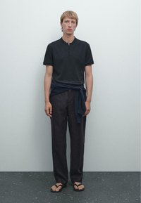 Sort polo-shirt med korte ærmer og knaplukning, parret med løse navybukser. Sorte flip-flops. Enkel, minimalistisk design.