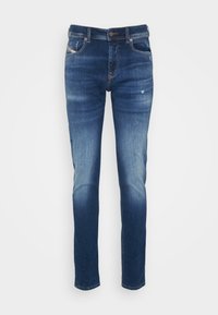 Jeans de mezclilla azul con un corte ajustado, que presentan un ligero desvanecimiento, pequeños detalles desgastados, un diseño tradicional de cinco bolsillos y trabillas para cinturón.