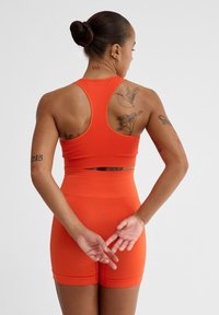 Pomarańczowy zestaw sportowy składający się z bezrękawowej crop topu i szortów o wysokim stanie. Gładka tekstura, dopasowany krój i brak widocznych wzorów.