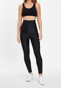 Svarta sömlösa högmidjade leggings med mjuk textur, kombinerade med en svart crop top och vita sneakers. Enkelt design, inga synliga mönster.