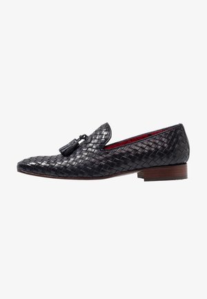 Mocasín negro de cuero trenzado con detalle de borla, tacón de madera bajo apilado y forro interior rojo.