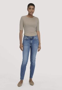 Beige aansluitend T-shirt met korte mouwen en een ronde halslijn, gecombineerd met strakke blauwe spijkerbroeken. Lichtbruine platte schoenen; gladde stoftextuur.