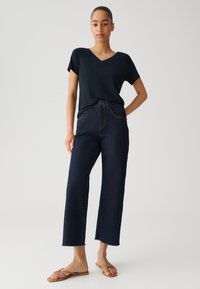 Navy V-Ausschnitt T-Shirt, entspannter Schnitt; hoch sitzende dunkelblaue Jeans, gerade Beinform mit ausgefranstem Saum; beigefarbene flache Sandalen. Einfaches und modernes Design.