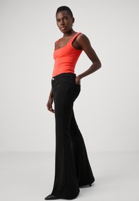 Top in arancione aderente con spalline larghe, abbinato a pantaloni neri svasati con tasche frontali e dettaglio con bottoni. Materiale liscio e elastico.