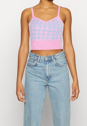 Femme portant un débardeur court en maille à carreaux roses et bleus, associé à un jean denim bleu clair taille haute.