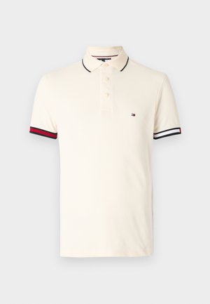 Polo shirt color beige chiaro con patta a due bottoni, colletto nero e maniche a coste con dettagli rossi e strisce bianche. Piccolo logo sul petto.