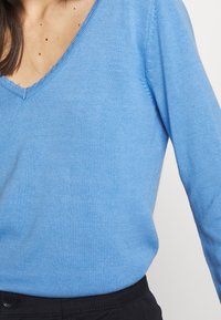 Hellblaues V-Ausschnitt-Sweatshirt aus Strickstoff mit glatter Textur, ausgestattet mit einem gerippten Kragen und Bündchen. Der Schnitt ist lässig, mit langen Ärmeln.