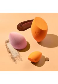 Trois éponges de maquillage roses et orange avec des traces de fond de teint liquide et en poudre sur une surface beige.