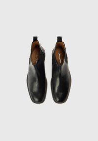 Černé kotníkové kožené boty s elastickými bočními panely, hladkou texturou, zaoblenou špičkou a hnědou štítkovou vložkou. Plochá gumová podrážka.