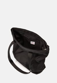 Sac fourre-tout noir avec fermeture éclair, en tissu, poche intérieure et deux poignées robustes. À l'intérieur, il y a une étiquette de logo.