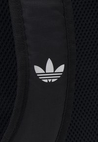 Black athletic bag featuring a textured mesh panel and a prominent white Adidas trefoil logo with three stripes below.