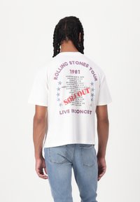 White cotton t-shirt featuring a retro Rolling Stones Tour design from 1981 on the back, with red text, blue stars, and "SOLD OUT" label.