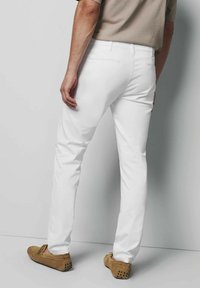 Witte slim-fit broek van een katoenmix, met een soepele textuur en standaardzakken. Draagt met tan kleurige suède schoenen, tegen een neutrale achtergrond.