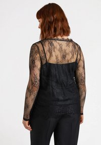 Top in pizzo nero con maniche lunghe, caratterizzato da un motivo floreale trasparente e uno strato sottostante nero opaco. Design testurizzato e aderente.