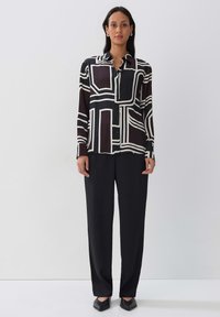 Long-sleeve blouse with a geometric black and white pattern, made of lightweight fabric, paired with black wide-leg trousers and flat shoes.