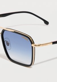 Gafas de sol con lentillas cuadradas de gradiente azul, montura negra y dorada, y logo "Carrera" en la lente y la patilla.