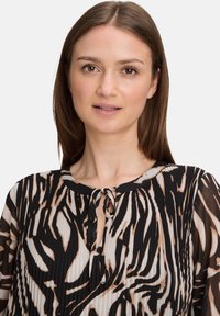 Bluzka z długim rękawem w czarno-beżowy wzór zwierzęcy, z plisowanym wzorem, okrągłym dekoltem oraz detalem w postaci wiązania z przodu.