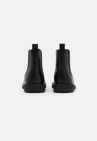 Bottines en cuir noir à finition lisse, panneaux latéraux élastiques, languettes de traction et semelle en caoutchouc texturée. Design minimaliste.