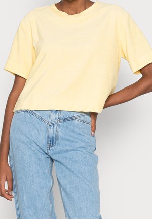 Żółta krótka koszulka, krótki rękaw, miękka tekstura, okrągły dekolt. Połączona z jasnoniebieskimi spodniami o wysokim stanie.