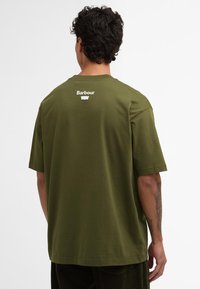 T-shirt en coton vert olive avec une coupe décontractée. Présente un logo Barbour blanc au dos. Manches courtes et texture lisse.