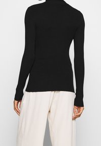 Haut noir côtelé à manches longues avec un col montant, une coupe ajustée et un tissu texturé ; associé à un pantalon large de couleur claire.