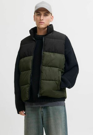 Gepolsterte Weste in Schwarz und Olivgrün, mit hohem Kragen, Reißverschluss, Seitentaschen und einem strukturierten schwarzen Pullover darunter.