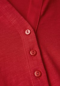 Cardigan rosso realizzato in tessuto testurizzato, con scollatura a V e quattro bottoni abbinati lungo la parte anteriore per la chiusura.
