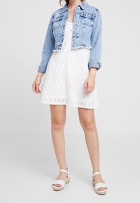 Denimkortjacka, ljusblå, med knappstängning och två bröstfickor. Vit klänning med texturerat blommönster. Vita espadrillosandaler.