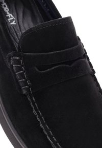 Mocasines de ante negro con acentos de costura decorativa, punta redonda y textura suave. Presentan un diseño sin cierre y costuras en contraste.