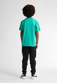 Grøn bomulds t-shirt med korte ærmer, kombineret med sorte sweatpants. Model iført hvide sneakers med sorte detaljer.