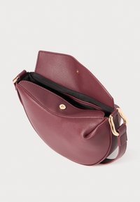 Sac à bandoulière en cuir bordeaux, forme incurvée, surface texturée, intérieur noir, fermeture à rabat magnétique, accents en métal doré.