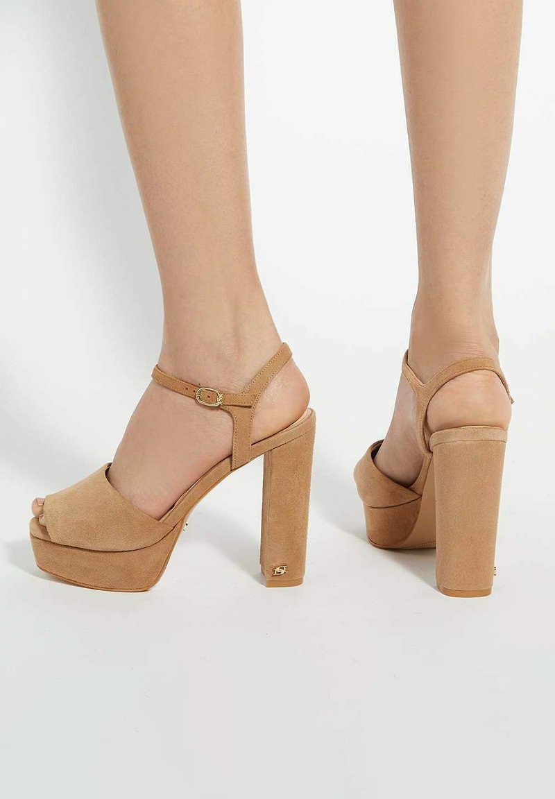 Beige suede platform sandals with a peep toe, ankle strap, and chunky high heel. Features a gold accent on the heel.
