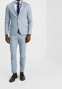 Jasnoniebieski garnitur w kratę o dopasowanym kroju, zestawiony z białą koszulą w kwiatowy wzór i granatowym krawatem. Błyszczące brązowe buty dopełniają całość.