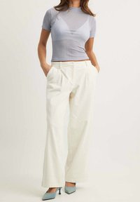 Ljusblå ribbad kortärmad topp som kombineras med högmidjade, vida cremefärgade byxor. Blå spetsiga klackar. Byxorna har en subtil textur och veck.