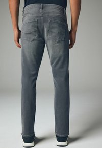 Szare dżinsy o prostym kroju, z dwiema tylnymi kieszeniami i detalami szycia. W zestawieniu z czarnym obuwiem.