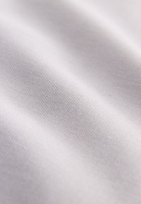 Close-up van glad, wit stof met fijne textuur en subtiele plooien die het zachte, geweven materiaaldetails laten zien.