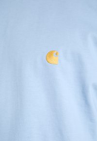 Light blue cotton t-shirt featuring a small, embroidered orange logo on the left chest area. The fabric has a smooth texture.