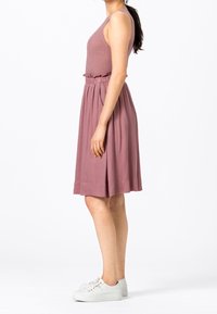 Pletená tílko v mauve barvě, doplněné volnou sukní ke kolenům ve stejném odstínu. Model nosí bílé tenisky a ukazuje elastický pas.