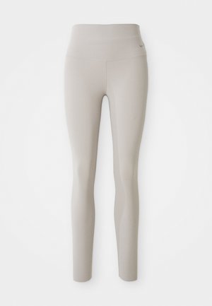 Beige high-waisted leggings made from stretchy fabric, featuring a form-fitting design and smooth texture, with a small logo on the waistband.