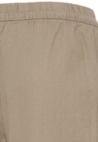 Tissu beige avec ceinture élastique et coutures visibles, montrant un gros plan du matériau de pantalons ou shorts décontractés.