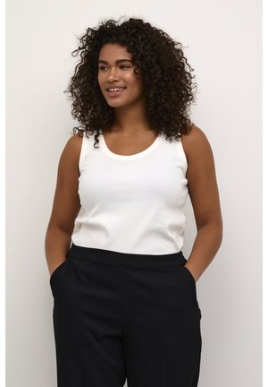 Weißes ärmelloses Tanktop mit rundem Halsausschnitt, aus weichem Stoff. Kombiniert mit hochgeschnittenen schwarzen Hosen mit Seitentaschen.