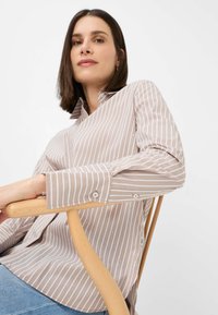 Striped beige shirt with buttons, featuring a collar and rhinestone accents. Designed with a relaxed fit and long sleeves.