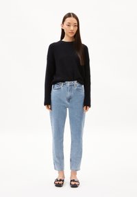 Un pull en maille noir, un jean taille haute bleu clair et des sandales à plateforme noires. La tenue présente une coupe décontractée et des détails minimalistes.