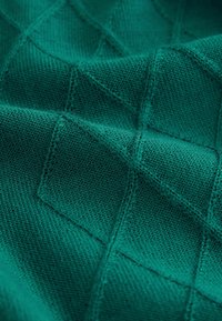 Türkisfarbenes Strickgewebe mit einem strukturierten Rautenmuster, glatt mit feinen Nahtdetails, das ein weiches, strukturiertes Erscheinungsbild erzeugt.