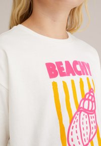 Balta medvilninė marškinėliai su spalvinga grafika, kurioje užrašyta "BEACHY" rožinėmis ir geltonomis vertikaliomis juostelėmis, bei rožinė kriauklė.