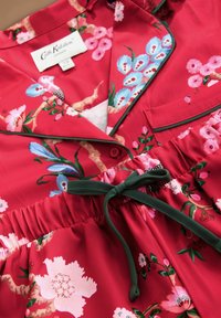 Rochie roșie cu flori roz și albastre, cu guler cu accente verzi, talie elastică și panglică legată la talie pentru ajustare.